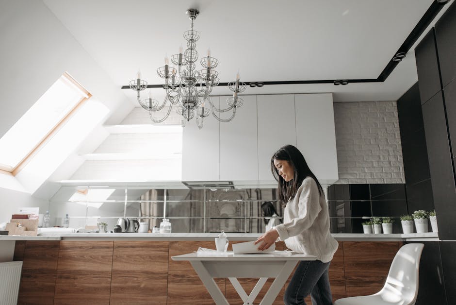 Une femme asiatique déballe des affaires dans une cuisine moderne avec des armoires en bois et un lustre.