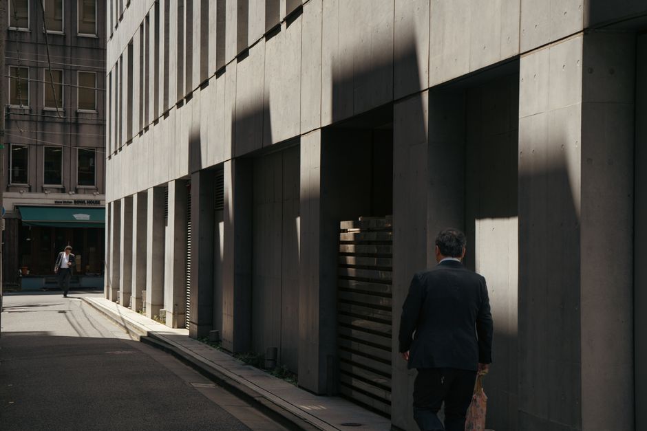 Ein Geschäftsmann geht in einer sonnendurchfluteten städtischen Gasse, ein Spiel aus Licht und Schatten in der Stadtaufnahme.