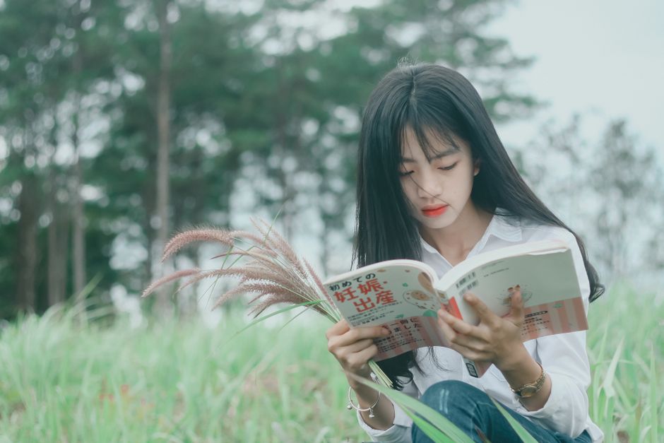 Asian woman reading a book outdoors, capturing a serene moment of relaxation in nature.