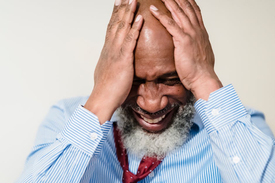 Elderly man in striped shirt showing stress and emotion with hands on head.