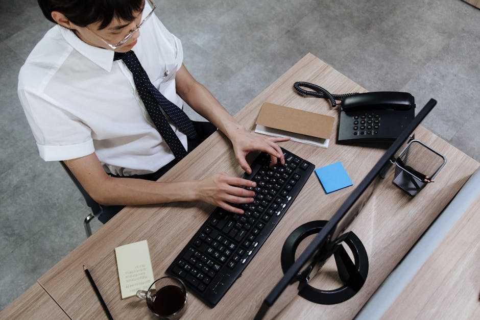Asian man in business attire typing on a keyboard at a modern office desk.