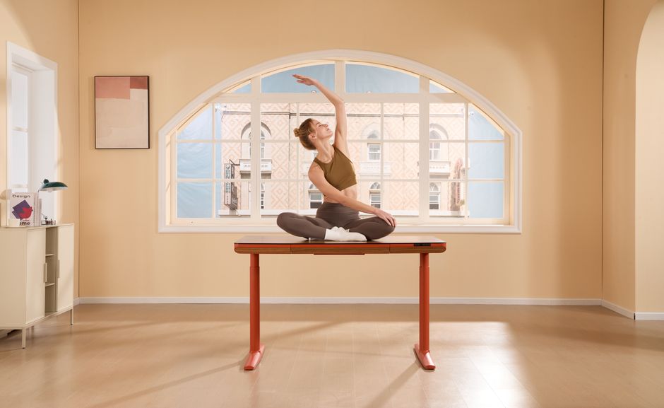 Woman practicing yoga on a desk in a bright, modern office with a large window.