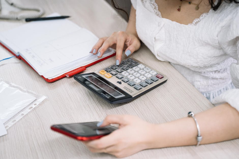 Close-up of a woman using a calculator and phone at her office desk.