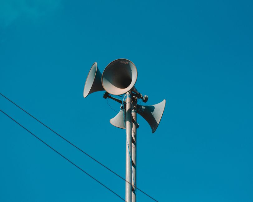 A set of loudspeakers on a pole against a bright blue sky, symbolizing communication and technology.