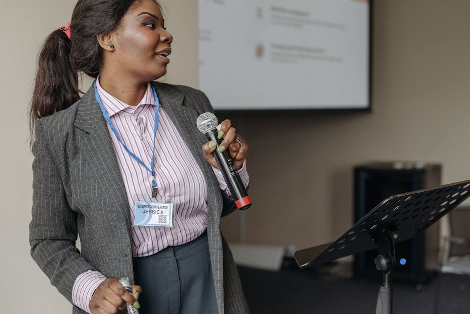 Woman in professional attire presenting at a business seminar with microphone.