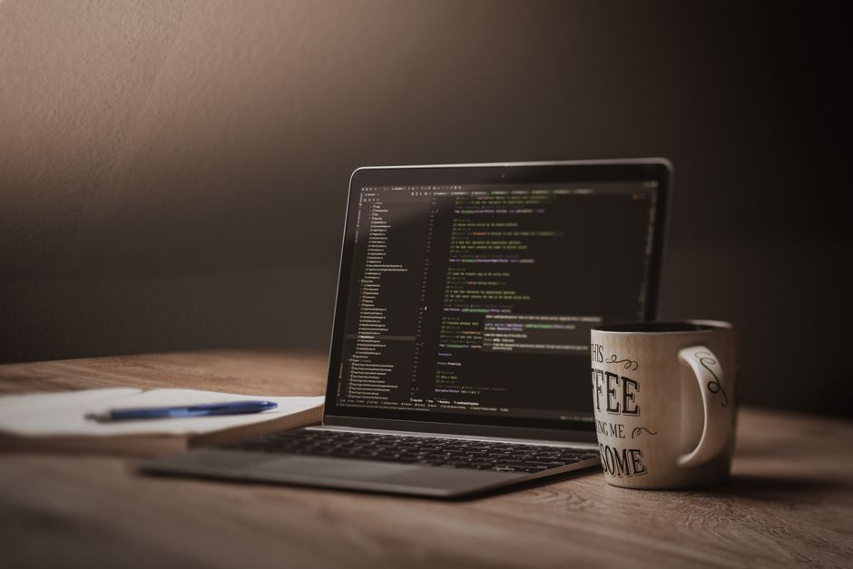 A comfortable workspace showcasing a laptop with code, a coffee mug, and a notepad.