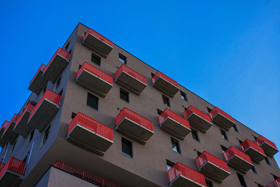 Low-angle view of a Vienna residential building with red balconies against a clear blue sky.