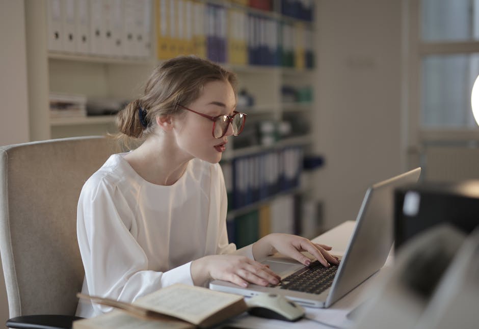 Professional woman in glasses working at a desk with a laptop in an organized modern office.