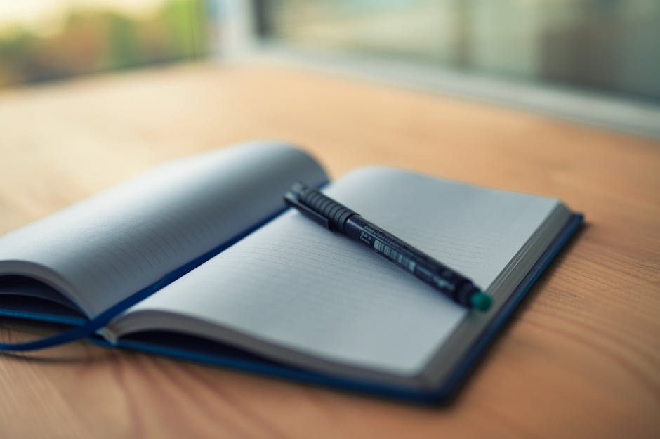 An open lined notebook with a pen resting on a wooden desk, capturing a moment of creativity.