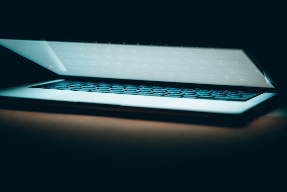 A close-up of a partially open laptop on a wooden surface, displayed in a moody lighting.